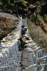 Randonnée au Népal tour de Manaslu : traversée d'un pont où sont accrochés des drapeaux de prières Akaoka