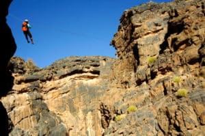 Kayak Oman : l'escalade d'un homme faisant de la tyrolienne dans un grand canyon d'Oman